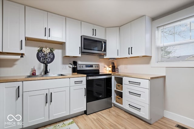 kitchen featuring white cabinetry, butcher block counters, stainless steel appliances, and light hardwood / wood-style flooring