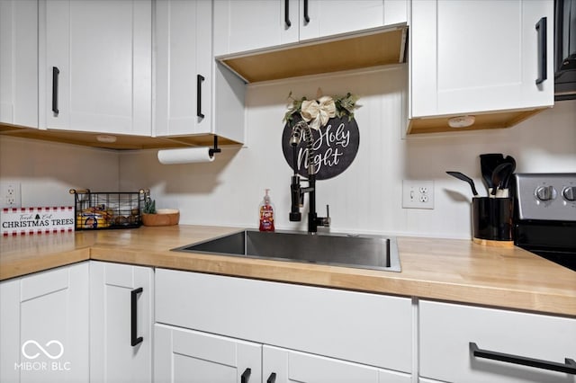 kitchen with wood counters, black stove, white cabinetry, and sink