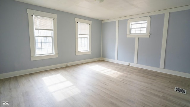 spare room featuring a healthy amount of sunlight, visible vents, baseboards, and wood finished floors