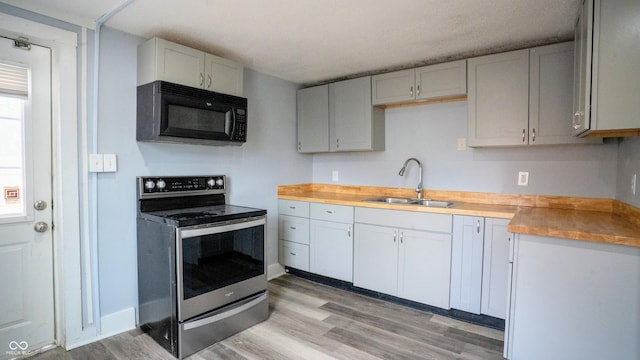 kitchen featuring stainless steel electric stove, light countertops, light wood-type flooring, black microwave, and a sink