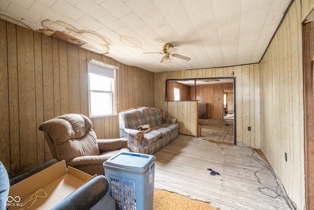 living area with ceiling fan and wooden walls