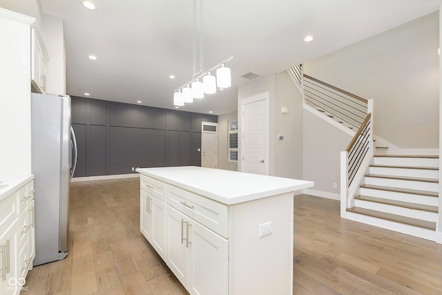 kitchen with white cabinets, stainless steel fridge, decorative light fixtures, and a kitchen island