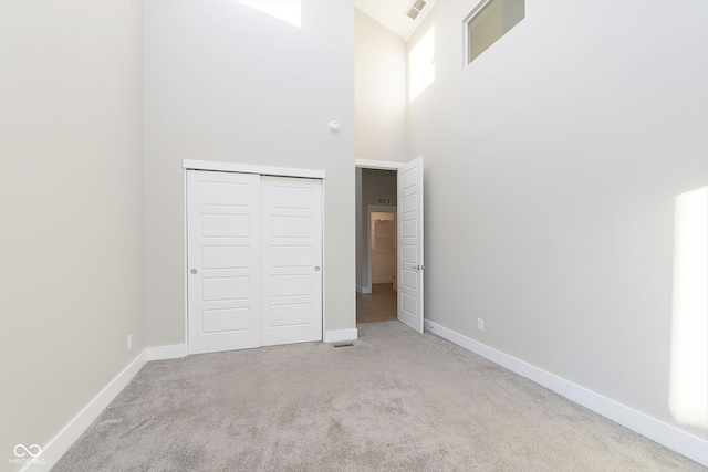 unfurnished bedroom featuring light colored carpet, a towering ceiling, and a closet