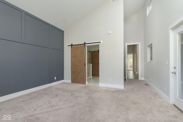 unfurnished bedroom with a barn door, a closet, high vaulted ceiling, and light colored carpet