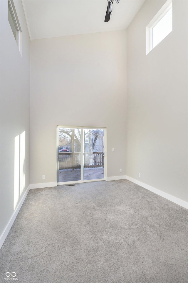 carpeted spare room featuring a high ceiling, plenty of natural light, and ceiling fan