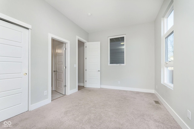 unfurnished bedroom featuring multiple windows, light carpet, and a closet