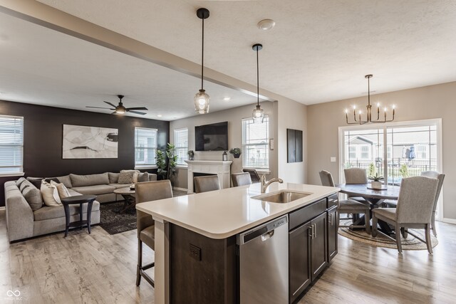 kitchen with sink, light hardwood / wood-style flooring, stainless steel dishwasher, pendant lighting, and a center island with sink