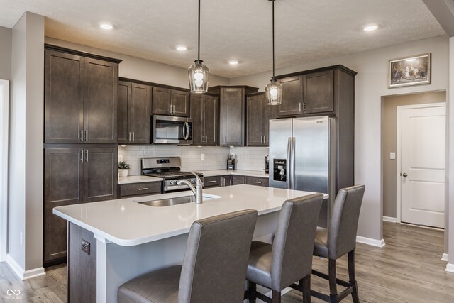 kitchen with hanging light fixtures, an island with sink, light hardwood / wood-style floors, a kitchen bar, and stainless steel appliances