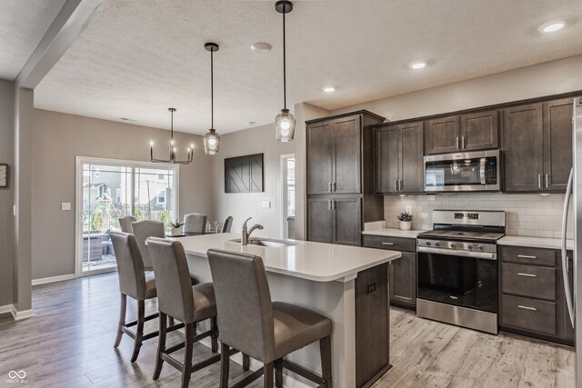 kitchen featuring a center island with sink, sink, hanging light fixtures, a breakfast bar area, and stainless steel appliances