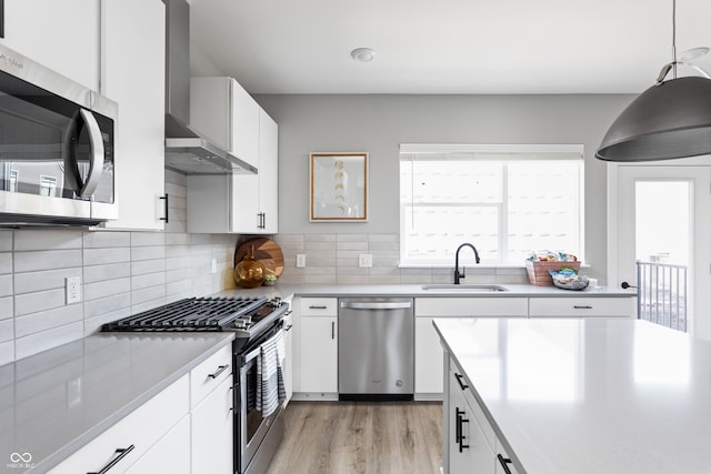 kitchen featuring white cabinetry, wall chimney exhaust hood, decorative light fixtures, and appliances with stainless steel finishes