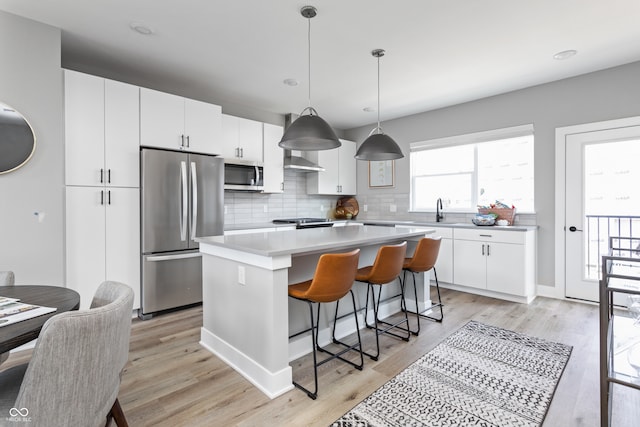 kitchen with pendant lighting, a kitchen island, stainless steel appliances, and light hardwood / wood-style floors