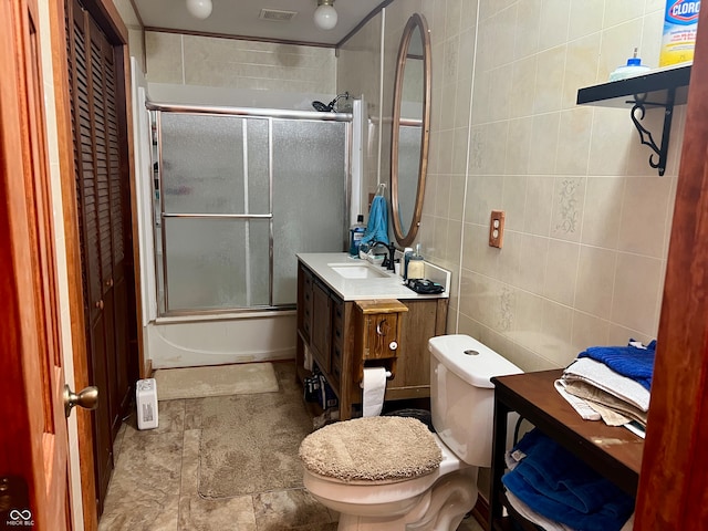 full bathroom with combined bath / shower with glass door, tile patterned floors, toilet, vanity, and tile walls