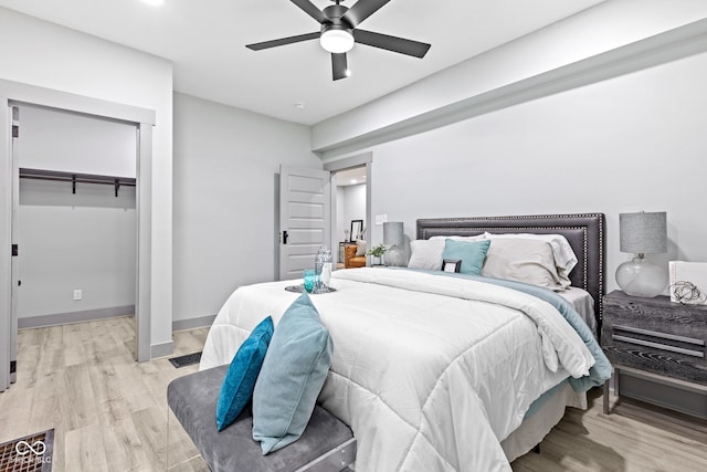 bedroom with light wood-type flooring, a closet, a spacious closet, and ceiling fan