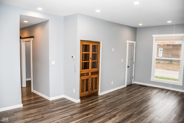 unfurnished room with a barn door and dark hardwood / wood-style floors