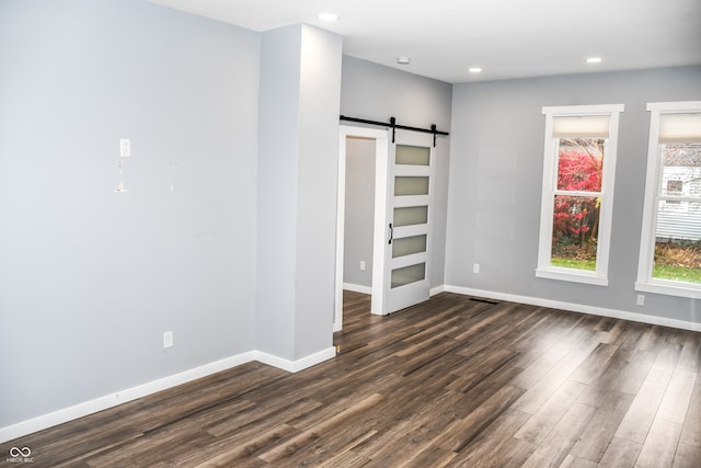 unfurnished bedroom with a barn door and dark hardwood / wood-style flooring