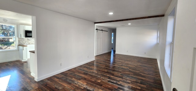 unfurnished bedroom featuring beam ceiling, a barn door, and dark wood-type flooring