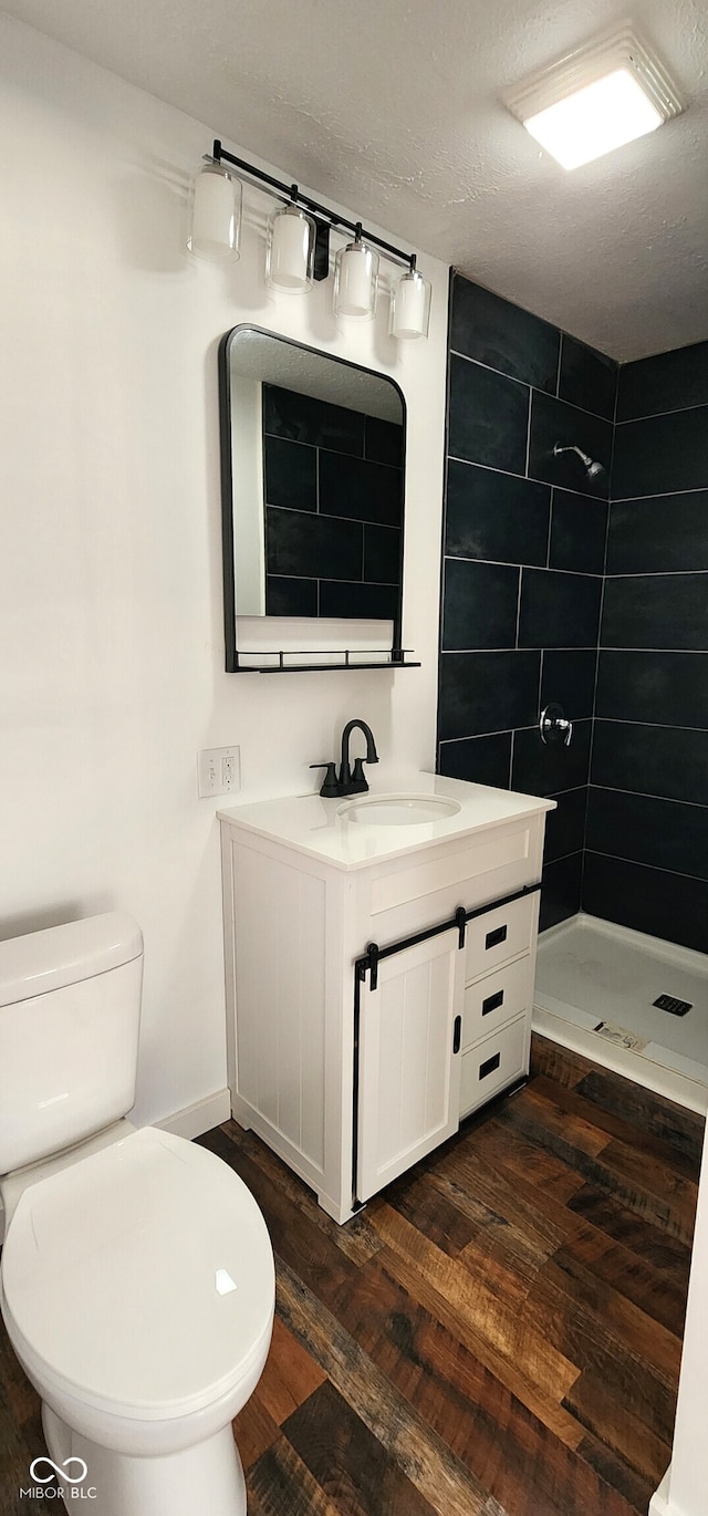 bathroom featuring vanity, a textured ceiling, tiled shower, hardwood / wood-style floors, and toilet