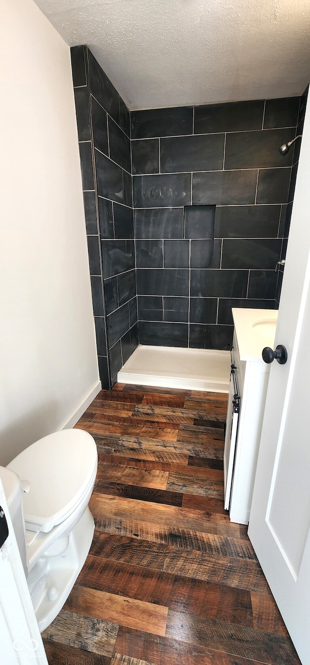 bathroom with a tile shower, vanity, a textured ceiling, wood-type flooring, and toilet