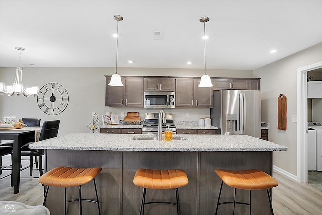 kitchen with a center island with sink, a kitchen breakfast bar, light hardwood / wood-style flooring, appliances with stainless steel finishes, and washing machine and clothes dryer