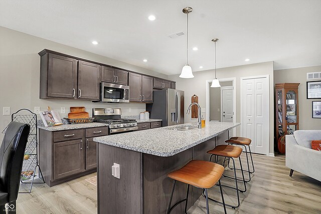 kitchen featuring dark brown cabinets, light wood-type flooring, an island with sink, and appliances with stainless steel finishes