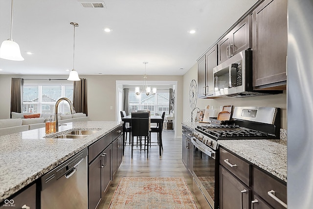 kitchen with sink, light wood-type flooring, dark brown cabinets, light stone counters, and stainless steel appliances