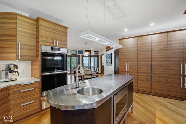 kitchen featuring sink, stainless steel microwave, hanging light fixtures, light hardwood / wood-style flooring, and double oven