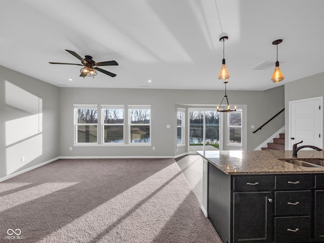 kitchen featuring dark stone counters, ceiling fan, sink, carpet floors, and hanging light fixtures