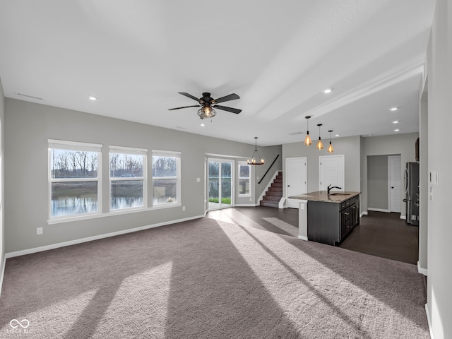 unfurnished living room featuring a wealth of natural light, sink, dark carpet, and ceiling fan with notable chandelier