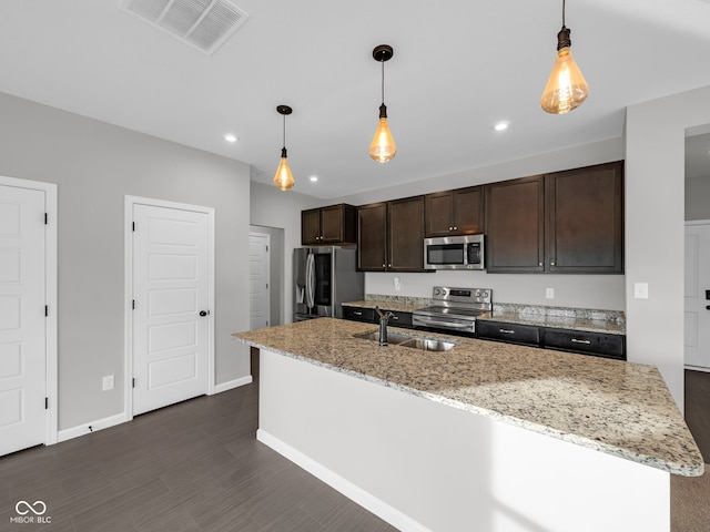 kitchen with light stone countertops, stainless steel appliances, sink, pendant lighting, and an island with sink