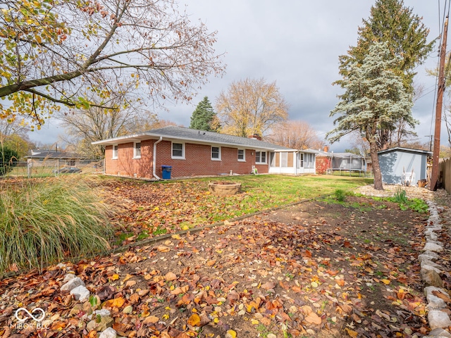 back of house featuring a sunroom, a storage unit, a trampoline, and a yard