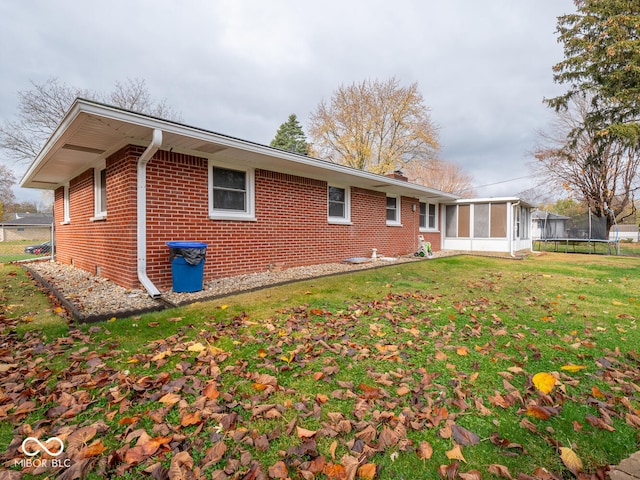 back of house featuring a sunroom, a trampoline, and a lawn