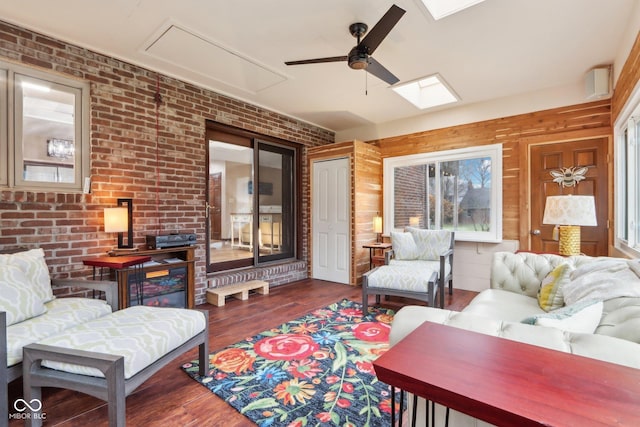 living room featuring ceiling fan, dark hardwood / wood-style flooring, brick wall, and a skylight