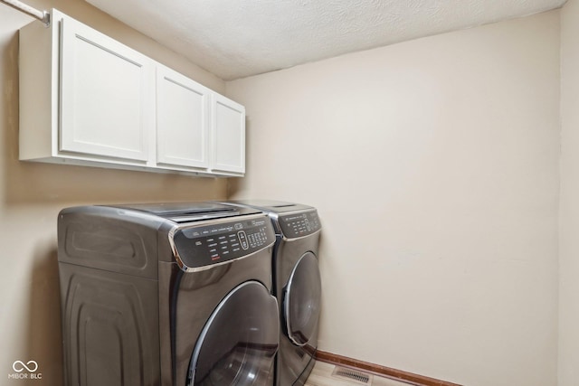 clothes washing area featuring cabinets, a textured ceiling, and washing machine and clothes dryer