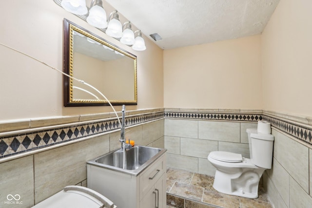 bathroom featuring a textured ceiling, vanity, tile walls, and toilet