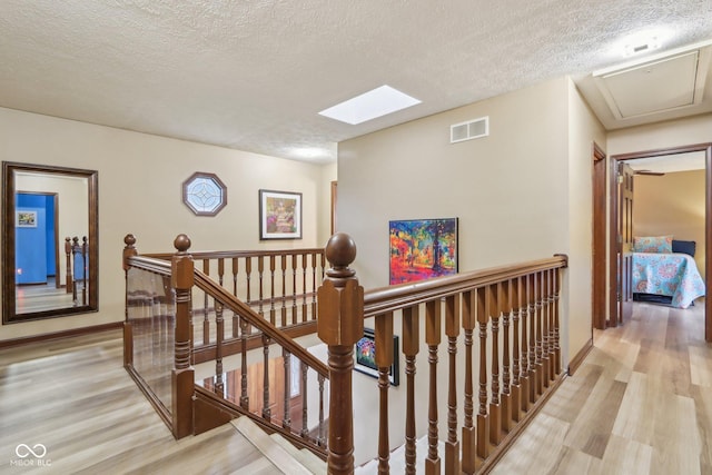 corridor with light hardwood / wood-style floors, a textured ceiling, and a skylight