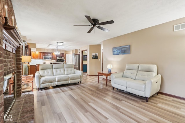 living room featuring ceiling fan, a fireplace, light hardwood / wood-style floors, and a textured ceiling