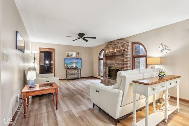 living room with ceiling fan, light wood-type flooring, and a brick fireplace