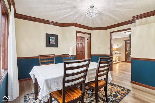 dining space featuring light hardwood / wood-style flooring, ornamental molding, a textured ceiling, and an inviting chandelier