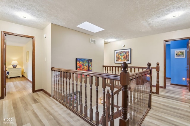 hallway featuring a skylight, light hardwood / wood-style floors, and a textured ceiling