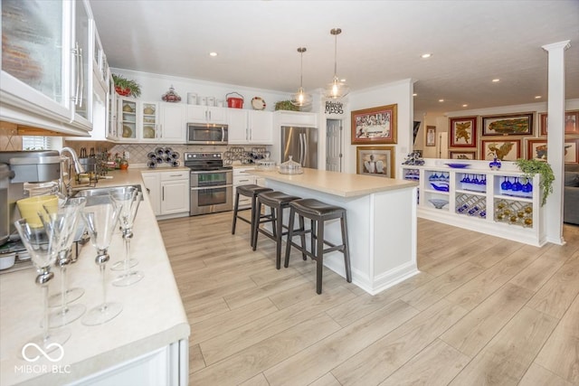 kitchen featuring white cabinetry, stainless steel appliances, light wood-type flooring, a kitchen island, and ornamental molding