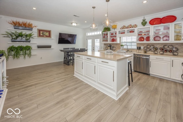 kitchen with decorative backsplash, stainless steel dishwasher, white cabinets, a kitchen island, and hanging light fixtures