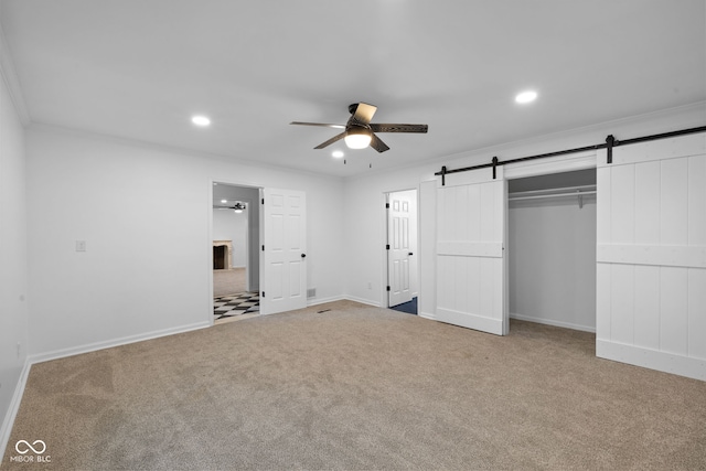 unfurnished bedroom with carpet, a barn door, a closet, and ornamental molding