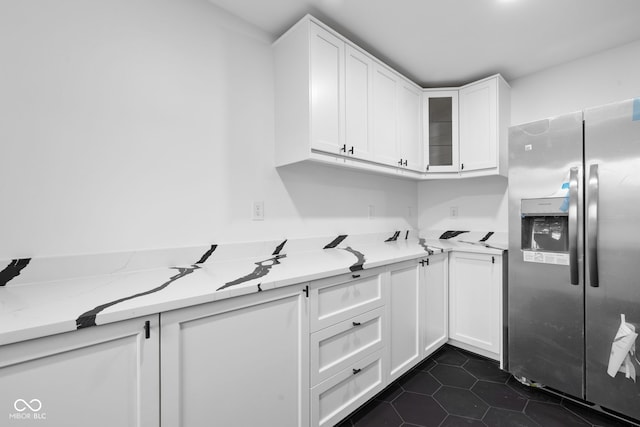 kitchen featuring white cabinetry, light stone counters, stainless steel fridge with ice dispenser, and dark tile patterned floors