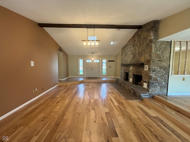 unfurnished living room featuring vaulted ceiling with beams, a stone fireplace, light hardwood / wood-style floors, and a notable chandelier