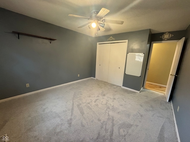 unfurnished bedroom featuring light carpet, a textured ceiling, a closet, and ceiling fan