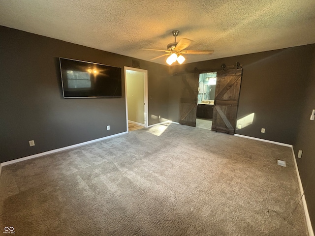 unfurnished room with carpet flooring, a textured ceiling, a barn door, and ceiling fan