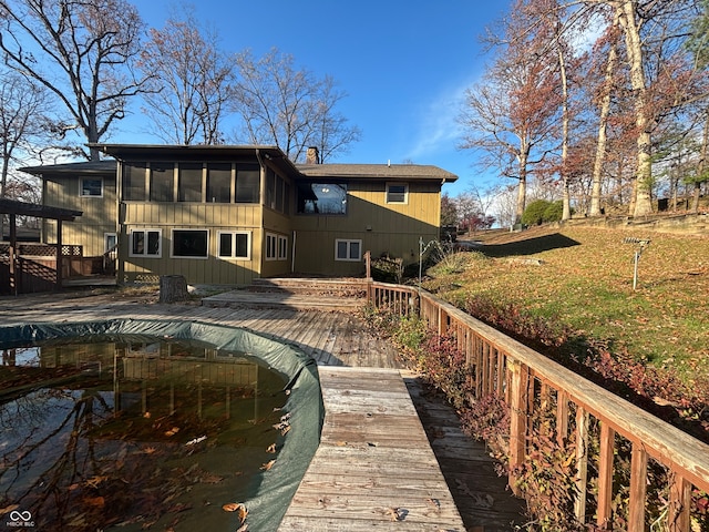 back of property with a sunroom, a wooden deck, and a lawn