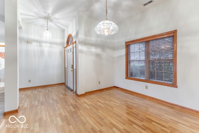 spare room featuring a notable chandelier and light hardwood / wood-style flooring