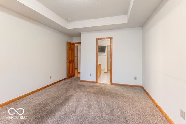 unfurnished bedroom with a raised ceiling, carpet floors, and ensuite bath