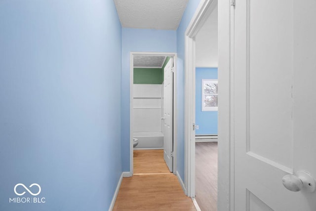 hallway with baseboard heating, light hardwood / wood-style floors, and a textured ceiling